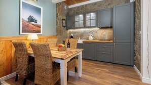 Un comedor con mesa de madera y sillas de mimbre, protector contra salpicaduras de piedra en la cocina y armarios grises.