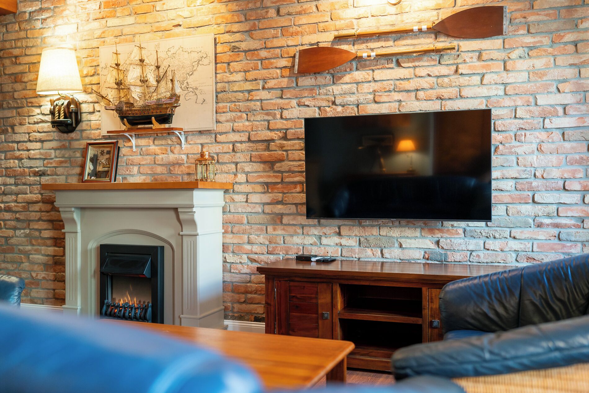 Ein Wohnzimmer mit Backsteinwand, Kamin, Wand-Fernseher und Ledersofa.