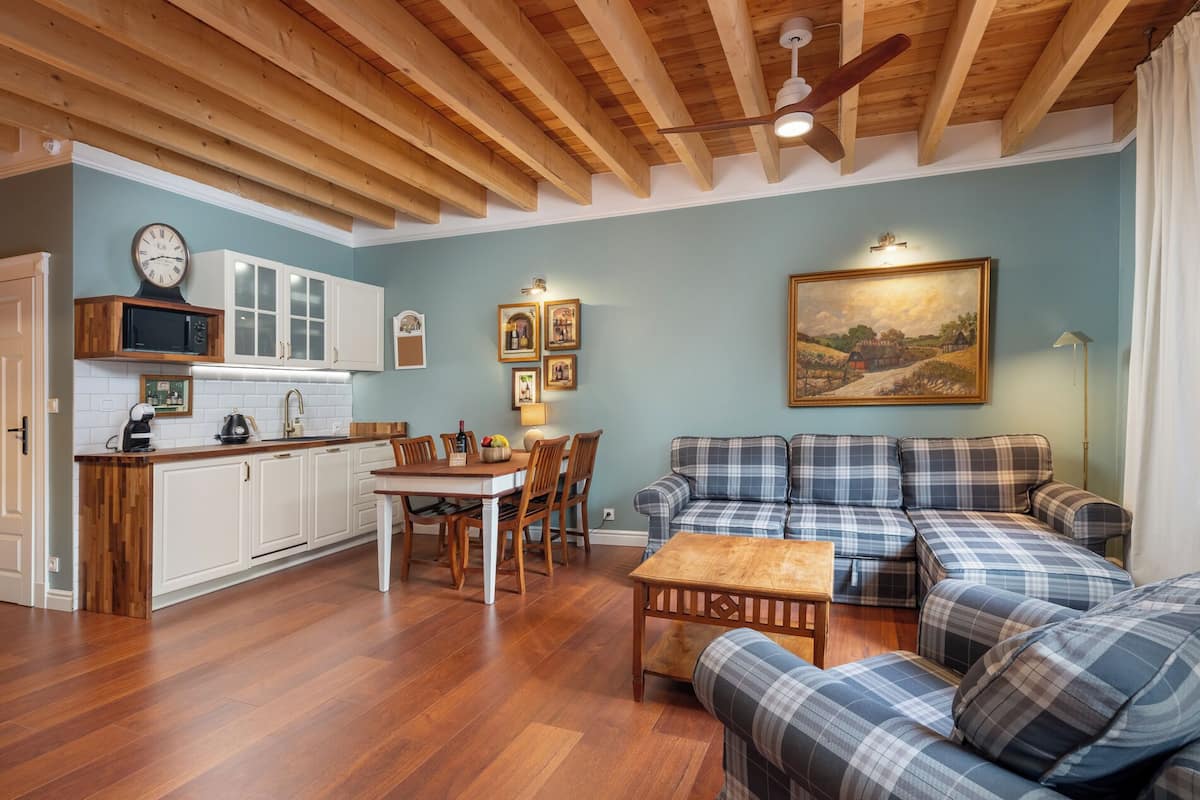 Amplia sala de estar con techo de madera, una mesa de comedor con sillas, un sofá y una zona de cocina con armarios y un reloj.