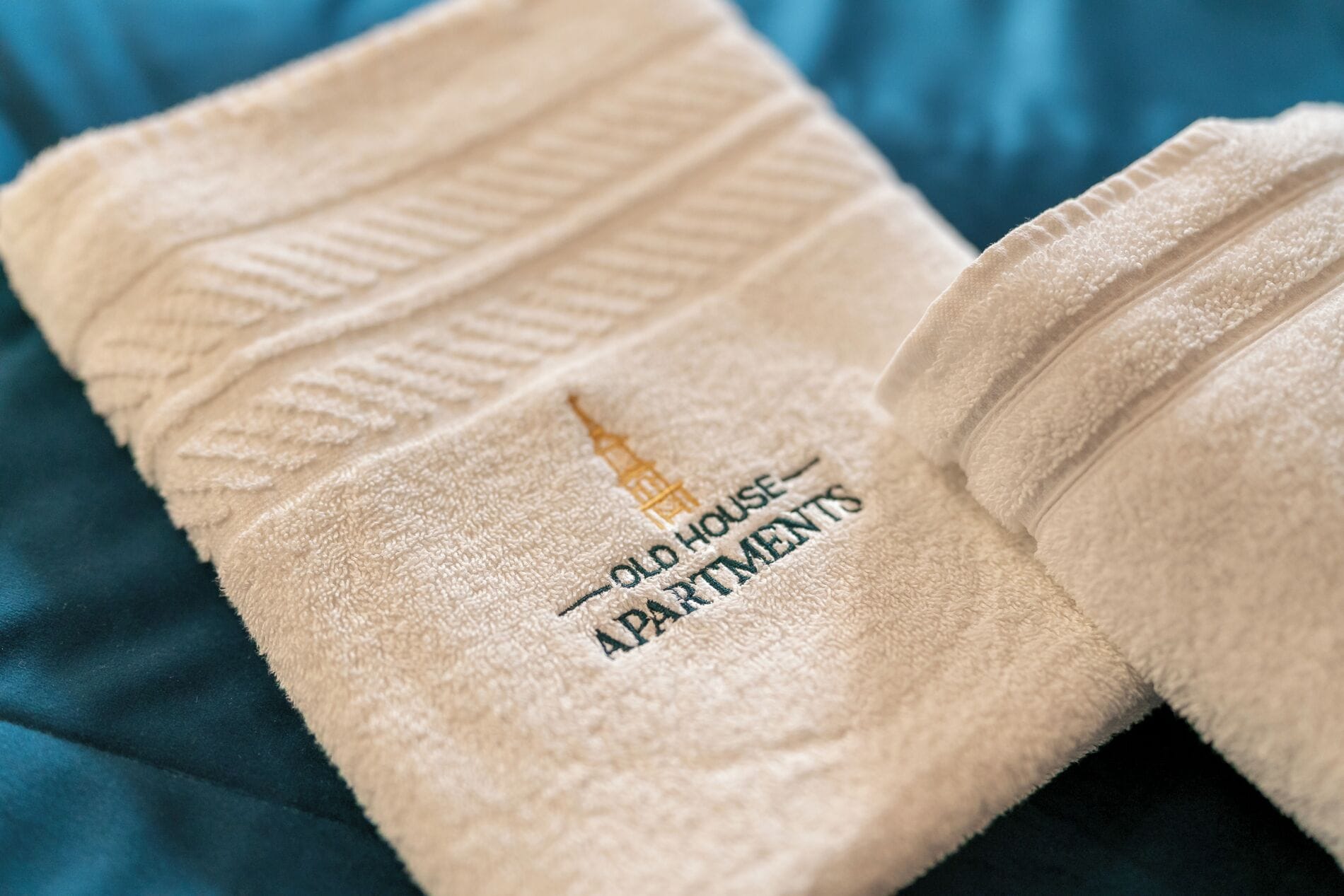 Een witte gevouwen handdoek met geborduurd tekst, dat het afkomstig is van 'Old House Apartments'.