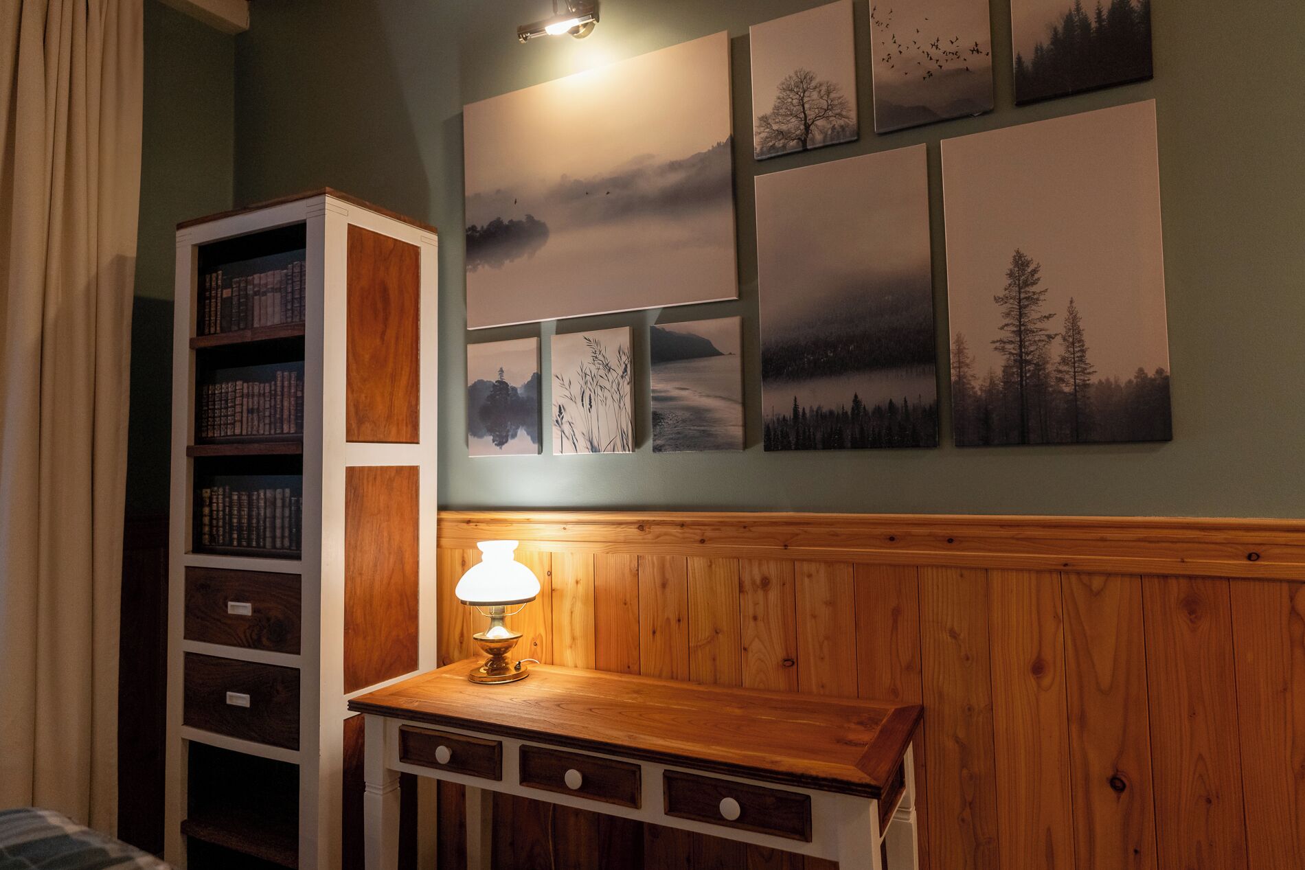 A room with a wooden cabinet, a table with a lamp, and a wall with multiple framed pictures.
