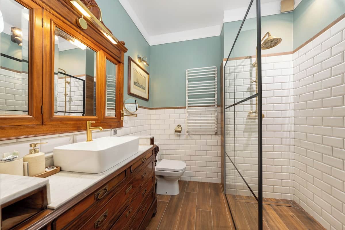 Un baño con tocador de madera, lavamanos blanco, inodoro y cabina de ducha con mampara de cristal.