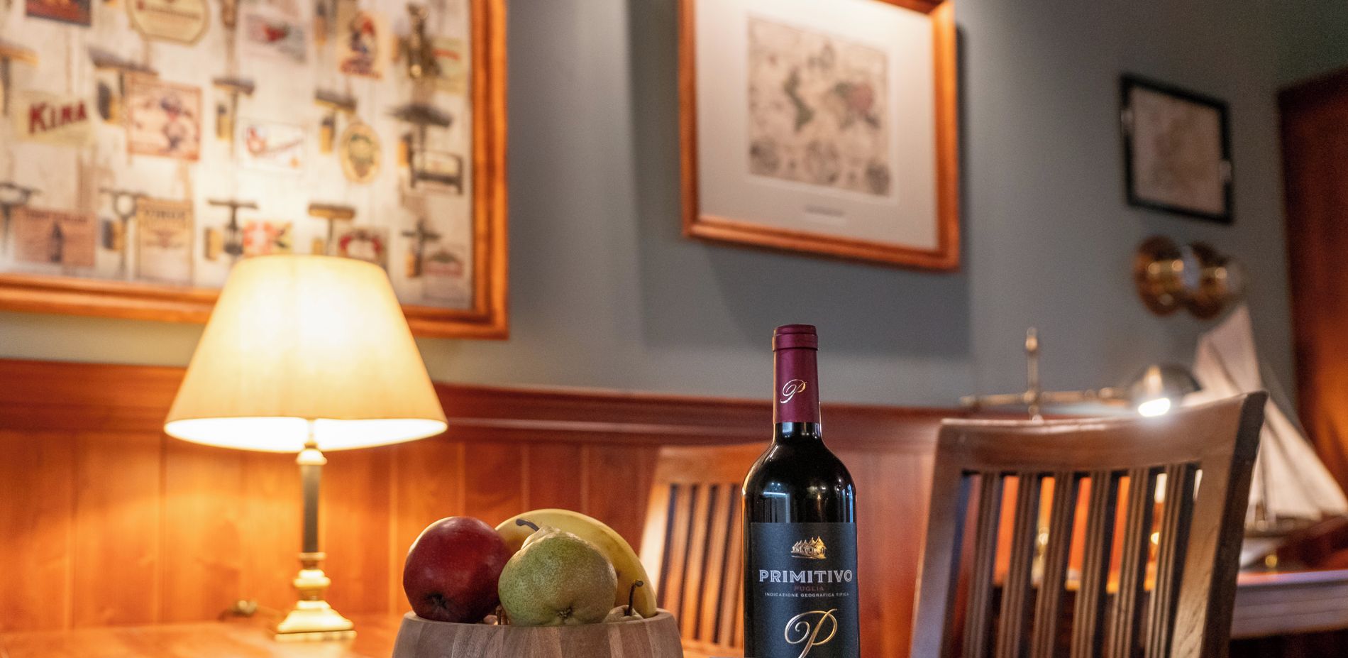 Une table en bois, une bouteille de vin, un saladier de fruits et une enseigne indiquant « Old House Apartments ».