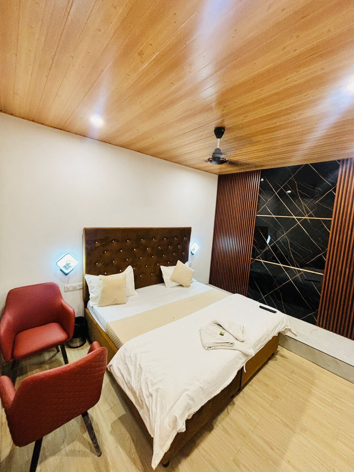 A bedroom with a wooden ceiling, a bed with white linens, a red chair, and a black and white patterned wall.