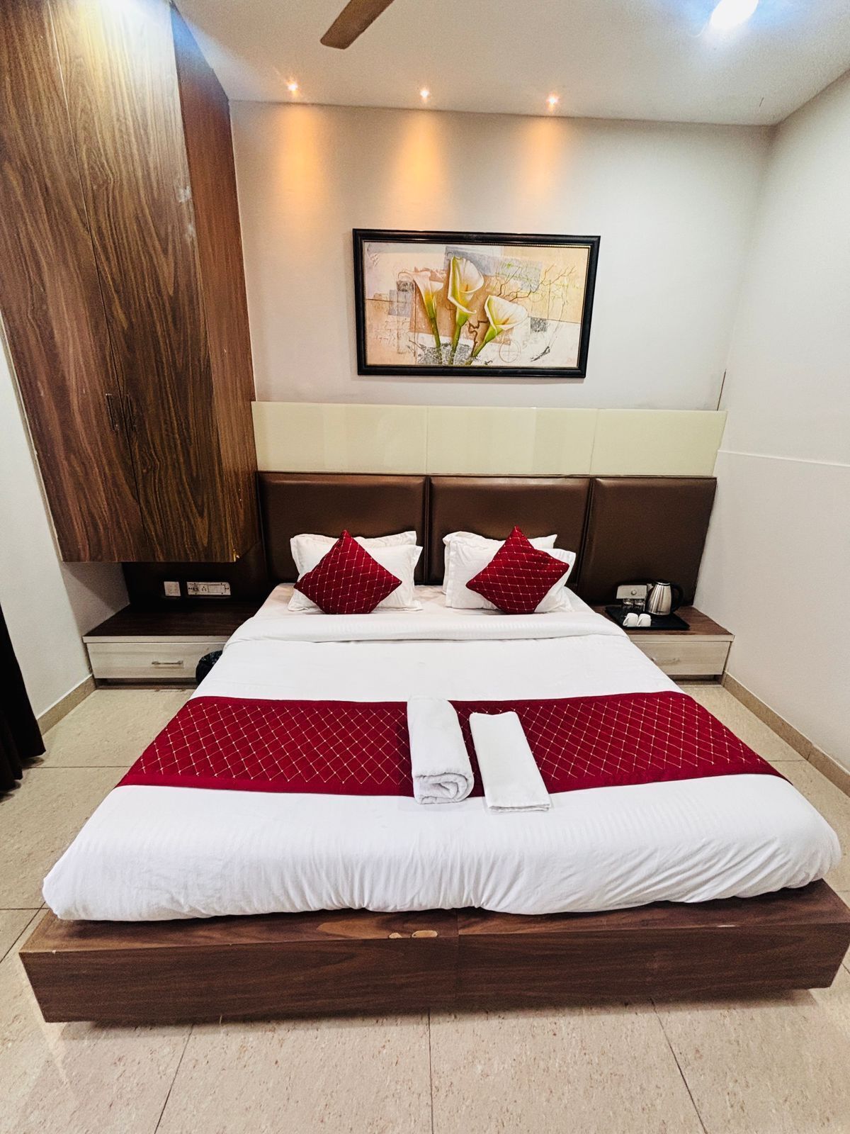 A hotel room with a large bed, two nightstands, a wooden headboard, a framed artwork on the wall, and a wooden wardrobe.