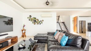 Una sala de estar moderna con un sofá de cuero negro, una mesa de centro de madera, un televisor de pantalla plana y un adorno de pared decorativo.