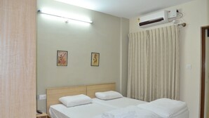 A hotel room with a bed, a bedside table, a wall-mounted air conditioner, and a curtain. - THE RED LOTUS GRAND (Mysore)