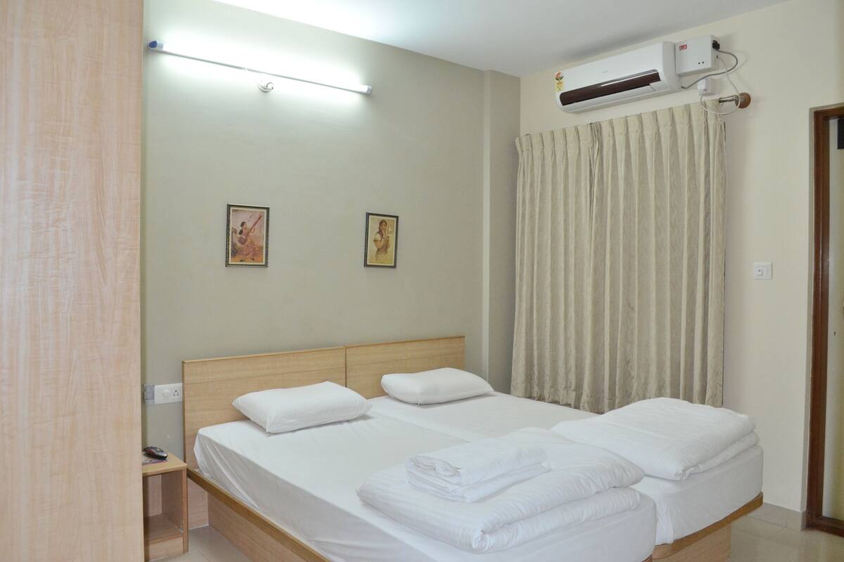 A hotel room with a bed, a bedside table, a wall-mounted air conditioner, and a curtain.