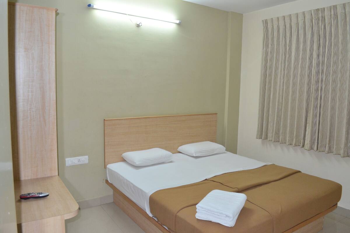A single bed with a wooden headboard, a brown blanket, and white pillows. A remote control is on a wooden nightstand beside the bed.
