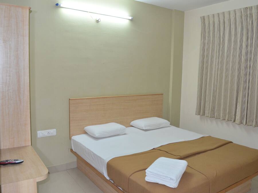 A single bed with a wooden headboard, a brown blanket, and white pillows. A remote control is on a wooden nightstand beside the bed.