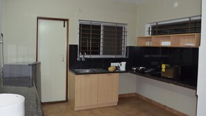 A compact kitchen with a refrigerator, sink, and wooden cabinets. - THE RED LOTUS GRAND (Mysore)