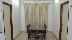 A dining area with a glass table and four chairs, a ceiling fan, and a curtain. - THE RED LOTUS GRAND (Mysore)