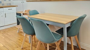 Moderni keittiö, jossa on puinen pöytä ja turkoosinsiniset tuolit, valkoinen kaappi ja seinälle asennettu valaisin.