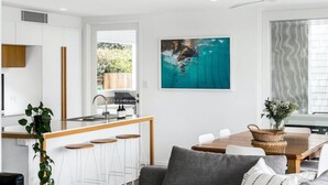 A modern kitchen with a central island, white bar stools, and a dining area with a wooden table and chairs.