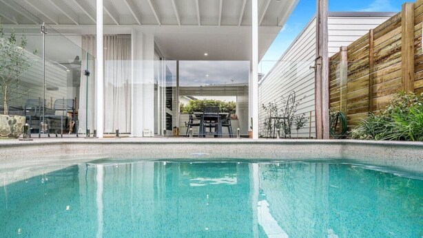 A swimming pool with a clear blue water surface, surrounded by a modern outdoor area with a covered seating area and a wooden fence.