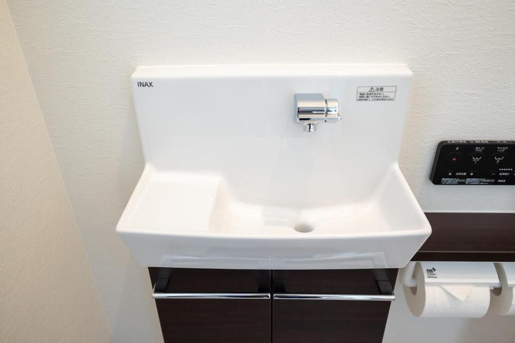 Un lavabo blanc pour la salle de bain, doté d’un robinet chromé, d’un panneau de commande avec du texte en japonais et d’un distributeur de papier toilette.