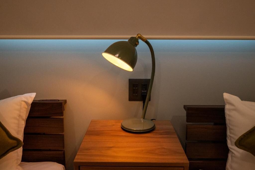 A wooden bedside table with a desk lamp, two nightstands, and a wall socket.