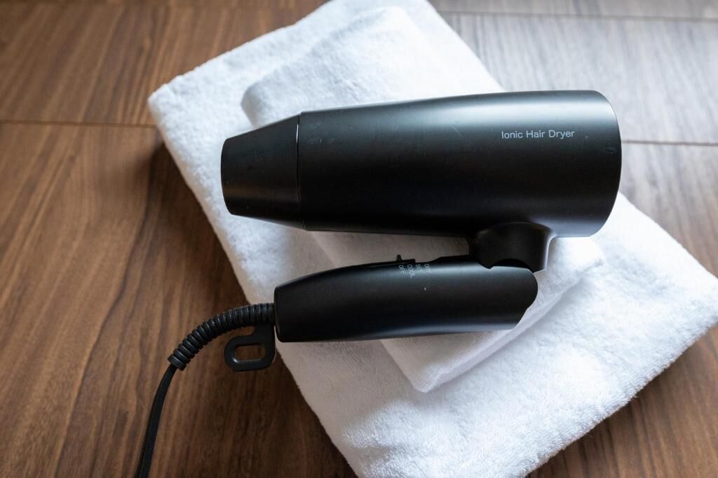 A black ionic hair dryer with a cord, placed on a white towel on a wooden floor.