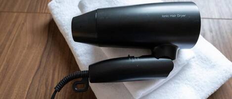 A black ionic hair dryer with a cord, placed on a white towel on a wooden floor.