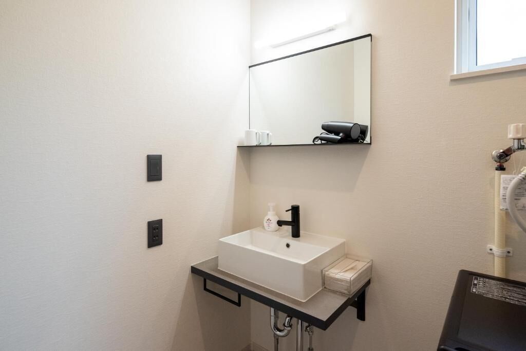 A modern bathroom with a white sink, black faucet, and a mirror above. There is a towel rack and a small shelf with a bottle.