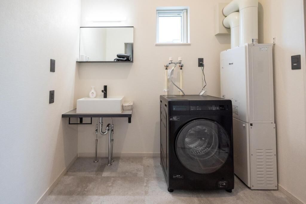 A compact laundry room with a washing machine, a sink, and a mirror.