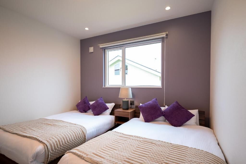 Habitación de hotel con dos camas, una ventana y una mesita de noche con lámpara.
