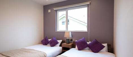 Habitación de hotel con dos camas, una ventana y una mesita de noche con lámpara.