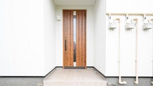 A wooden door in a hallway with white walls and tiled flooring.