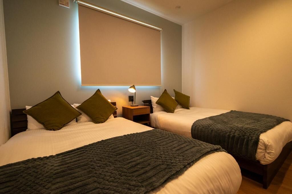 Une chambre d’hôtel avec deux lits, chacun recouvert d’une couverture vert foncé et agrémenté d’oreillers assortis.