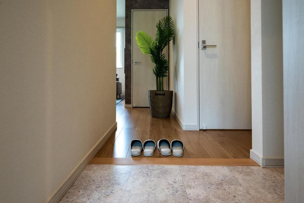 A hallway with a wooden floor, a potted plant, a trash bin, and a door.