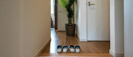 A hallway with a wooden floor, a potted plant, a trash bin, and a door.