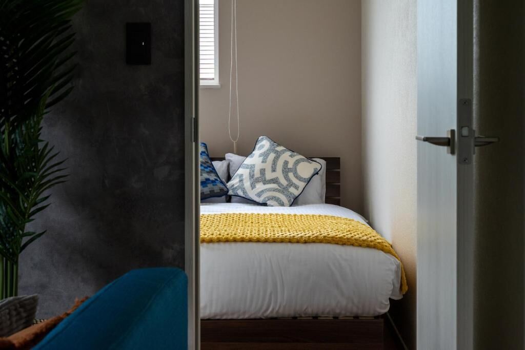 Een slaapkamer met een bed, kussens, een gele deken en een raam.