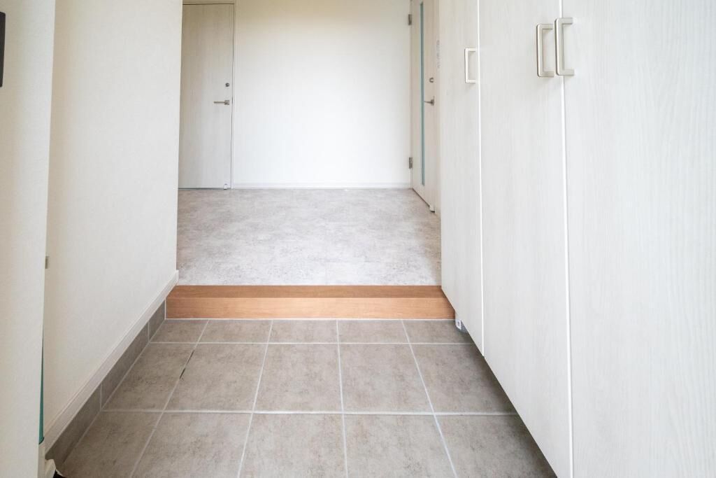 A hallway with a tiled floor, a wooden threshold, and white walls.