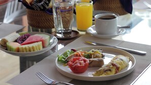 A breakfast setting with a plate of fruit, a glass of orange juice, a cup of coffee, and a basket of bread. - Dhanya Villa Lovina by Parigata (Buleleng)