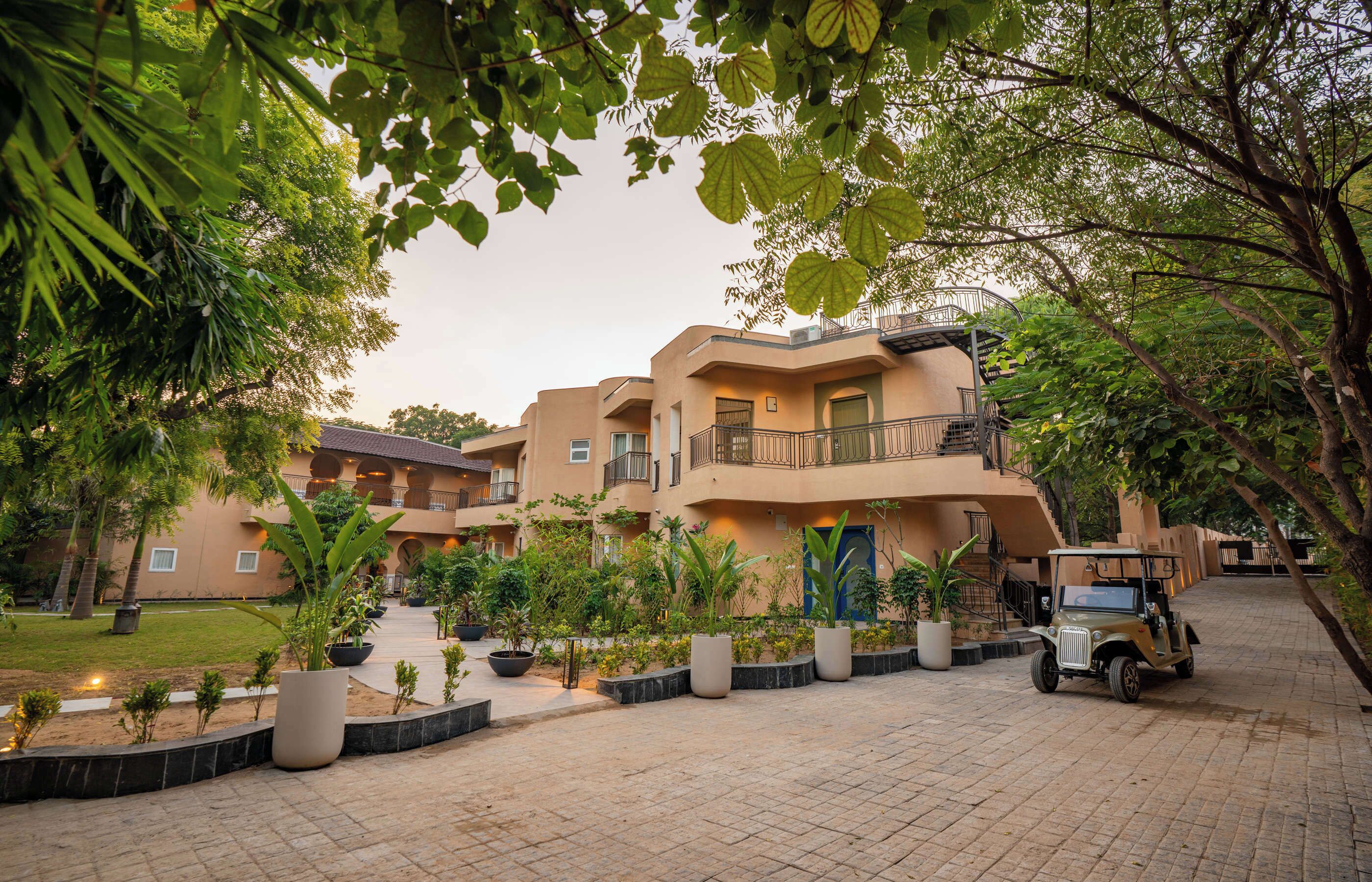 Un hotel de varios pisos con un patio, plantas en macetas y un vehículo estacionado.