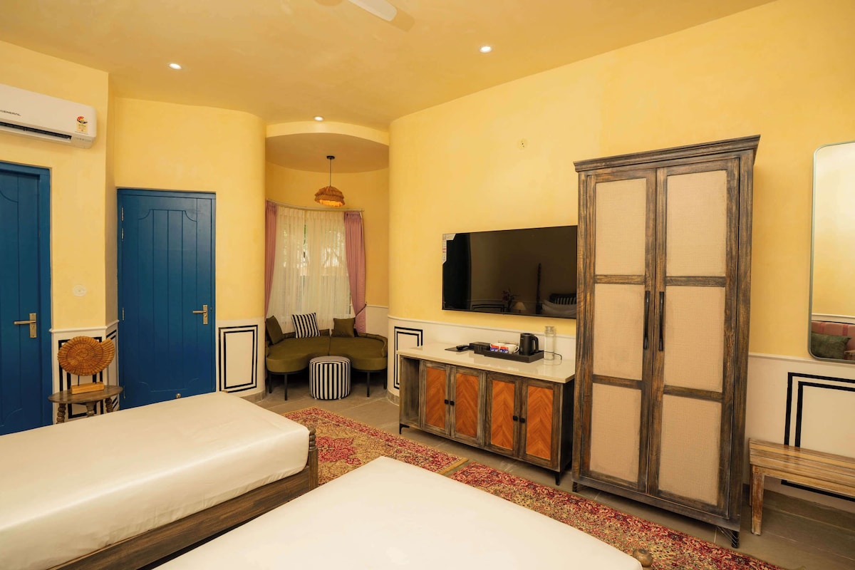 Una habitación de hotel con dos camas, un sofá, un televisor, un armario y una mesita.