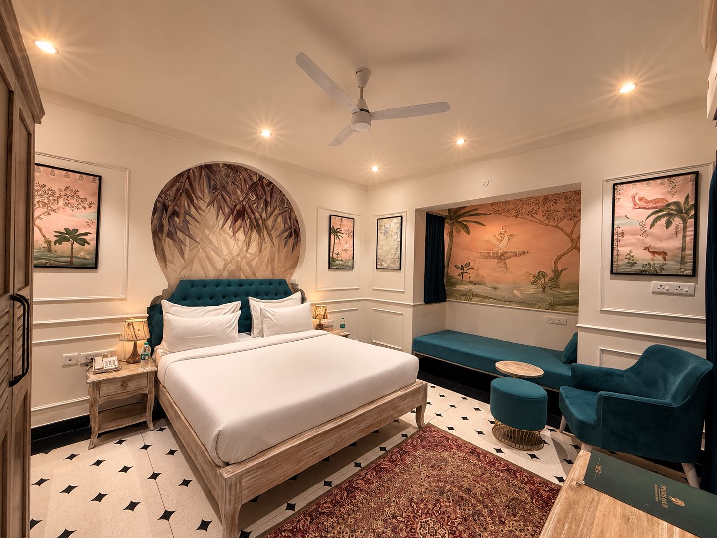 A bedroom with a large bed, a ceiling fan, a seating area with a sofa and armchairs, and artwork on the walls.
