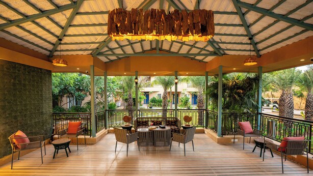 An outdoor patio with a wooden floor, a central round table, and multiple chairs. - Sisodia Bagh Luxury Boutique Resort (Amer)