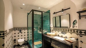 A bathroom with a glass-enclosed shower, a sink with a mirror, and a tiled floor with a geometric pattern. - Sisodia Bagh Luxury Boutique Resort (Amer)