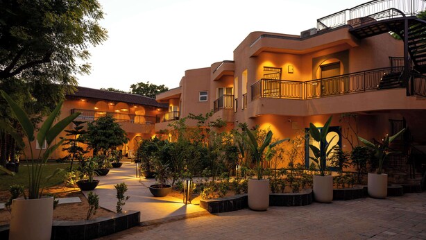 A multi-story hotel with a courtyard featuring potted plants and a central light fixture. - Sisodia Bagh Luxury Boutique Resort (Amer)
