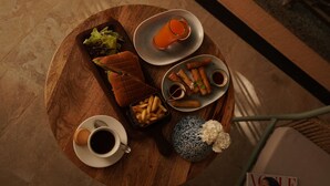 A round wooden table with a variety of food items including a sandwich, fries, spring rolls, and a glass of orange juice. There are also two cups of coffee and a decorative vase. - Sisodia Bagh Luxury Boutique Resort (Amer)