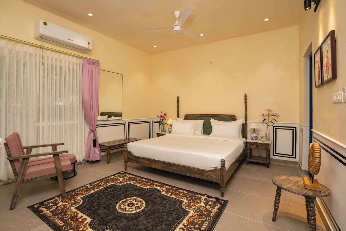 Un dormitorio con cama, una silla, una mesita de noche, aire acondicionado, ventilador de techo y una alfombra decorativa.