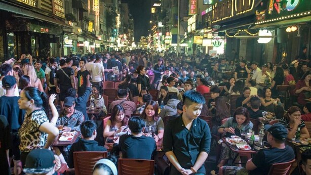 Una strada affollata con numerose persone che cenano a tavoli all'aperto.