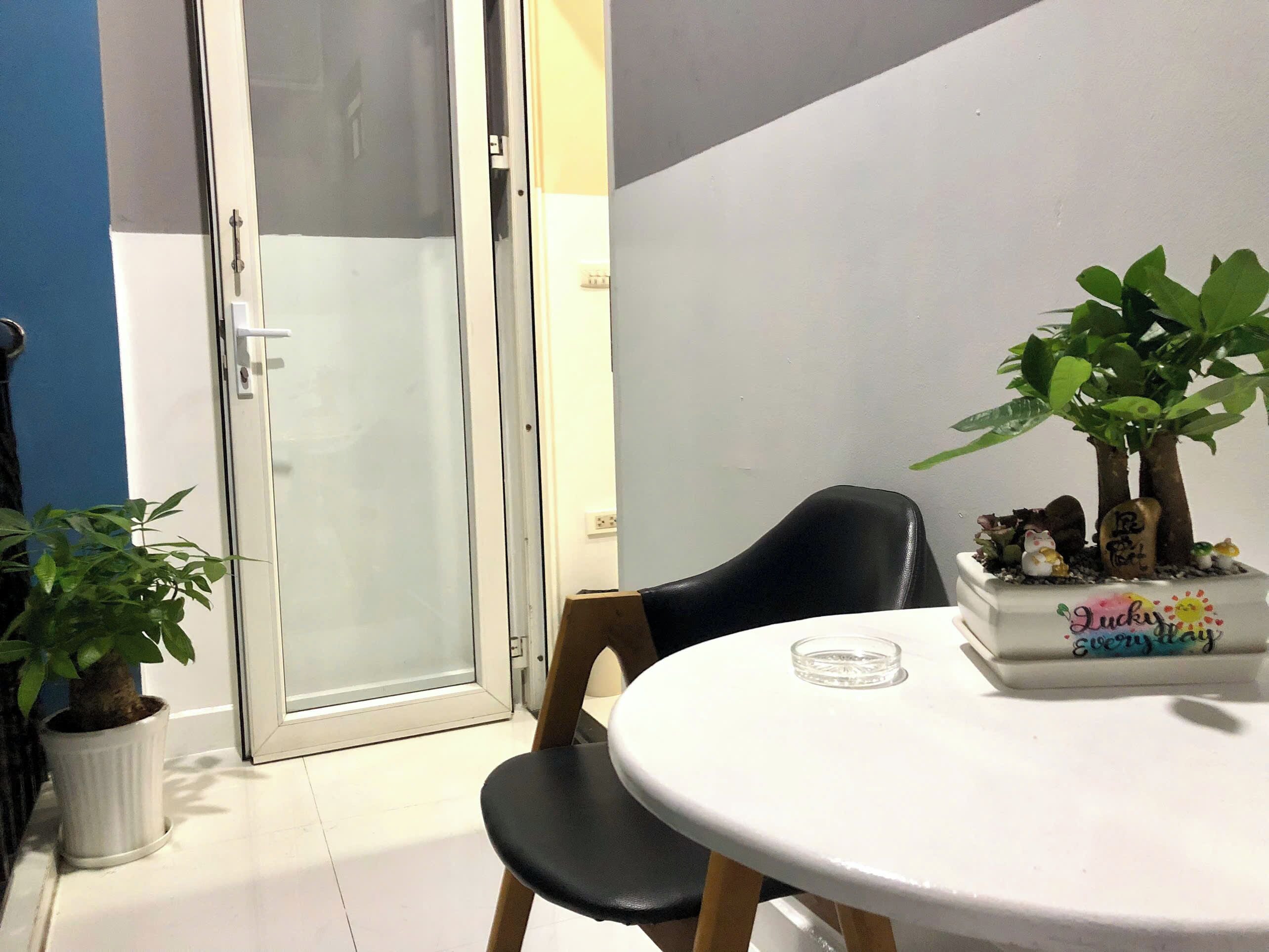 Una habitación con una mesa redonda, una silla negra, una planta en maceta y un búcaro decorativo con un mensaje.