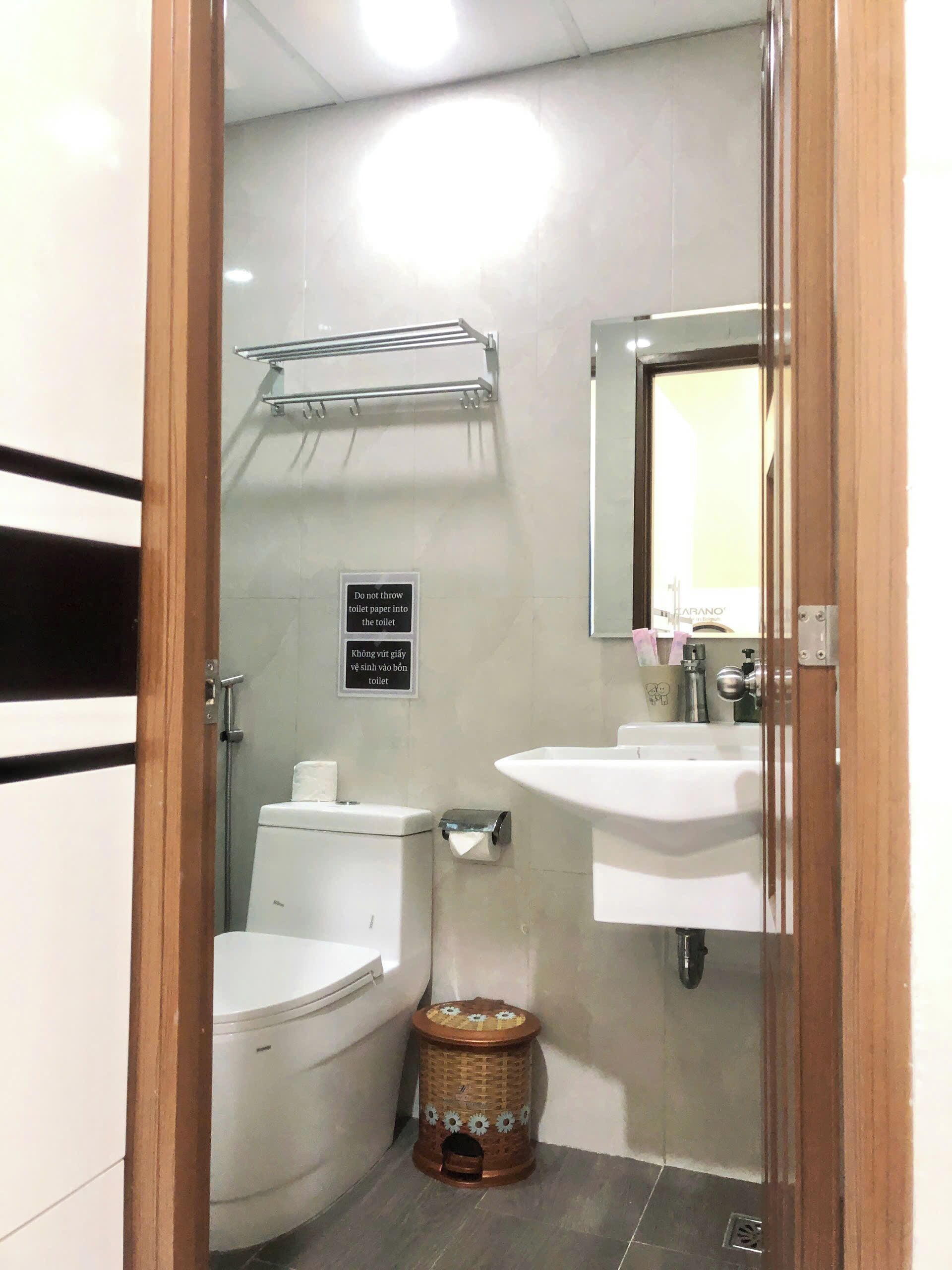 A small bathroom with a toilet, sink, and a trash bin. There is a sign instructing not to throw toilet paper into the toilet.