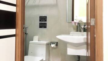 A small bathroom with a toilet, sink, and a trash bin. There is a sign instructing not to throw toilet paper into the toilet.
