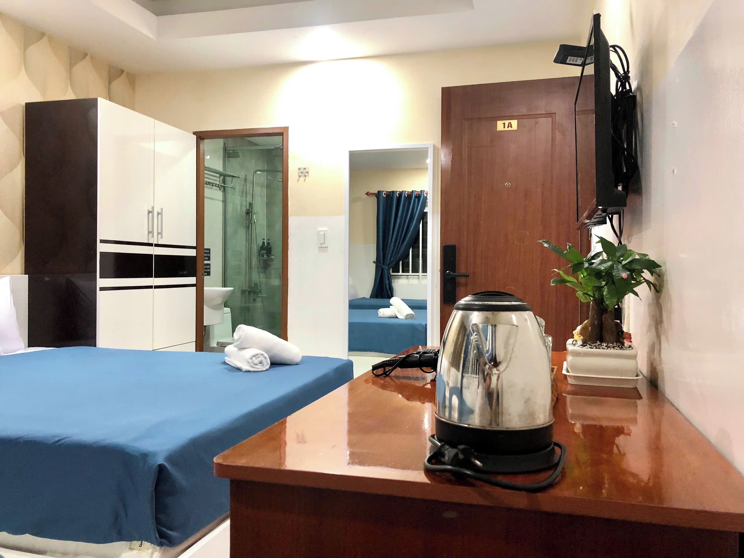 Een hotelkamer met een bed, een bureau met een waterkoker, een kamerplant en een kledingkast.