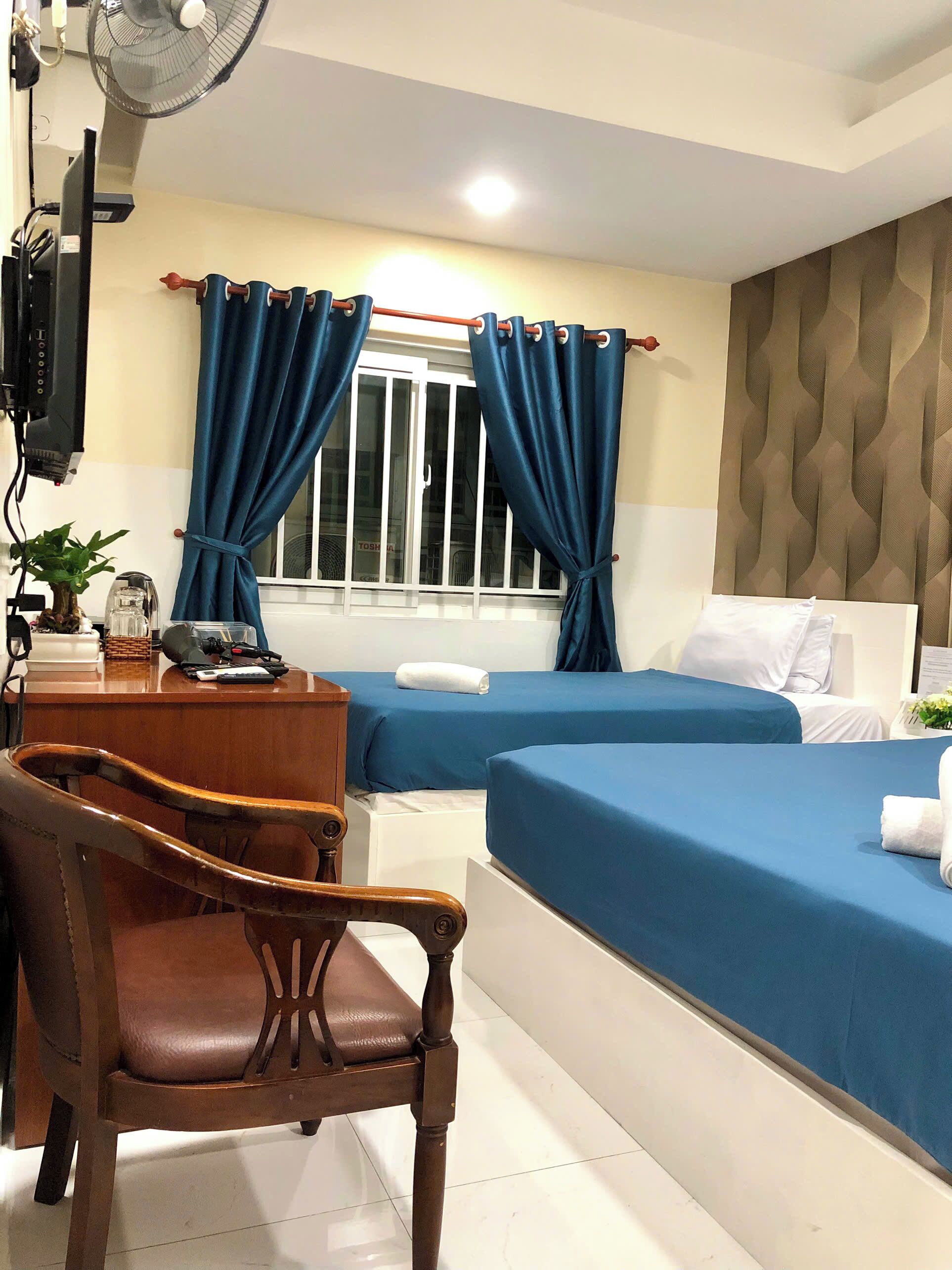 A hotel room with two beds, a desk with a chair, a TV, and a window with curtains.