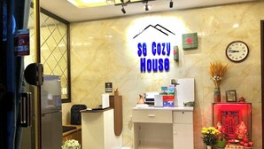 Zona reception di un hotel con un cartello che riporta "SG Cozy House", una sveglia e un piccolo santuario con offerte.