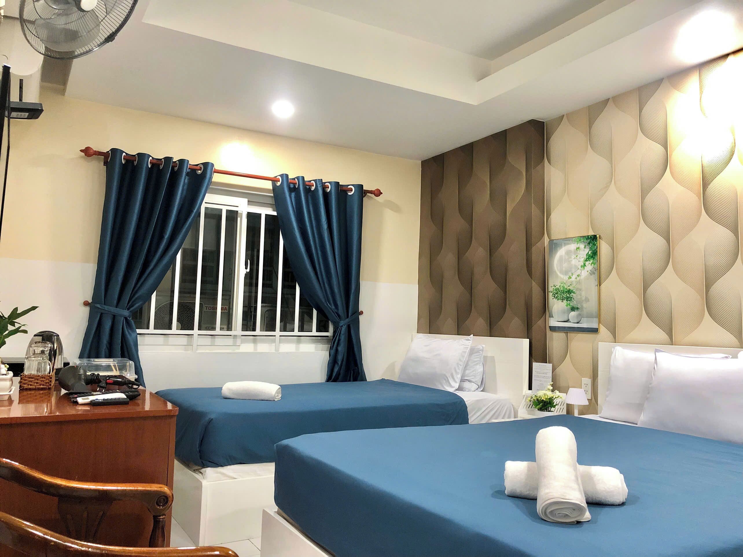 Habitación de hotel con dos camas, un escritorio, una silla, un ventilador y una ventana con cortinas.